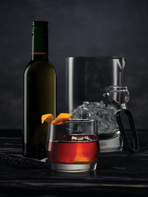 Cocktail mixing tools surrounding a Boulevardier on a dark surface